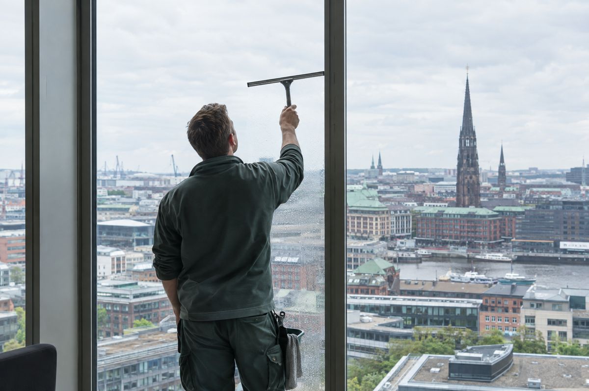 Glasreiniger zieht eine große Fensterscheibe mit Blick über Hamburg ab